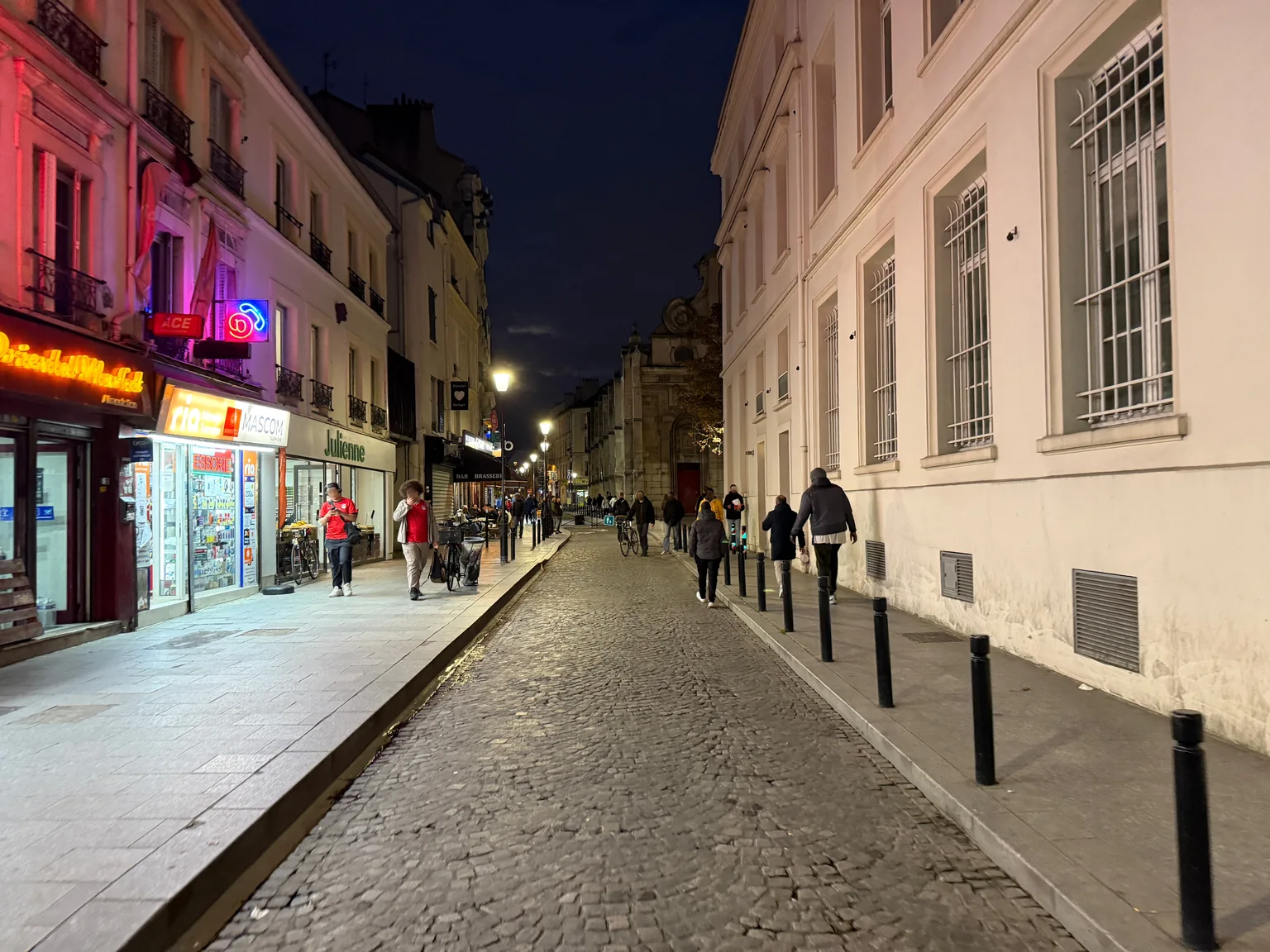 Rue du Moutier à Aubervilliers, avec ses immeubles, commerces et la rue pavée photographiés le soir.